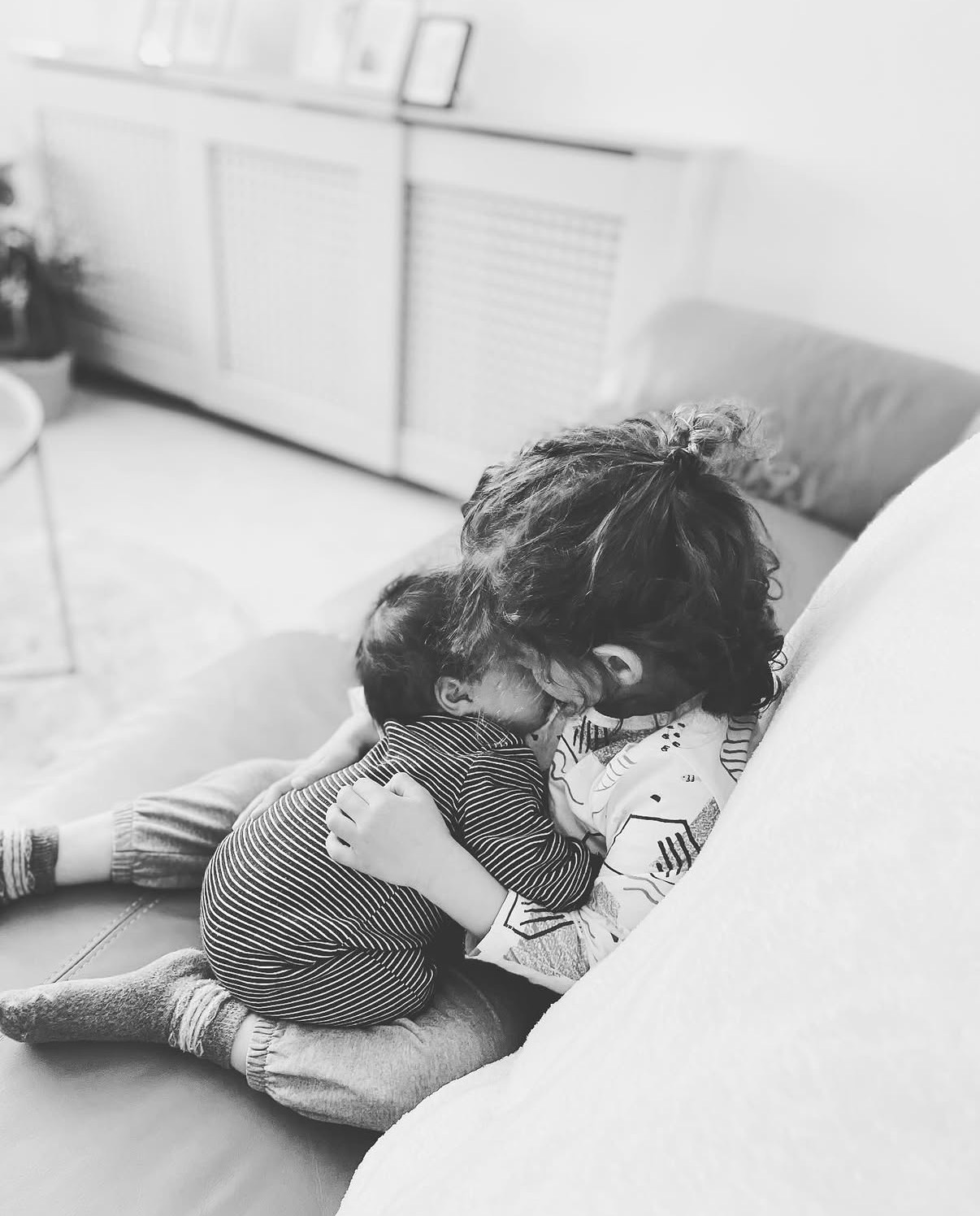 A young child holding a baby on the sofa, black and white photograph